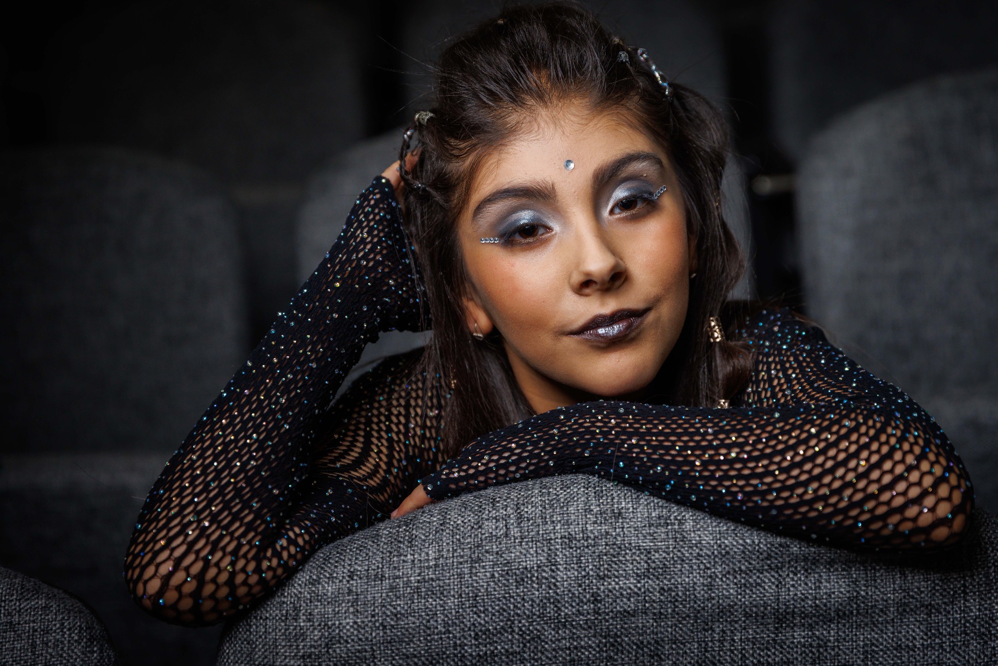 Una participante con maquillaje escénico apoya el rostro en una mano, sentada entre butacas.