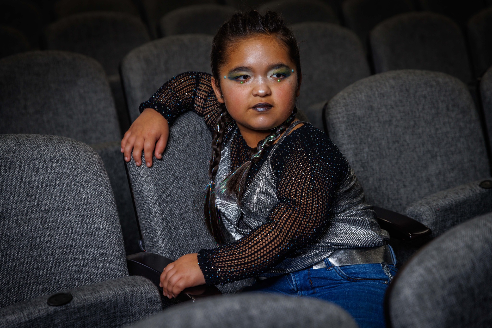 Una participante con maquillaje escénico está sentada entre las butacas de un teatro.
